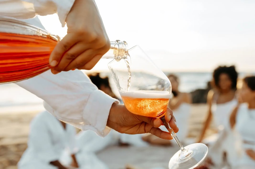 Close up of a drink being poured into a glass during a beach gathering at sunset